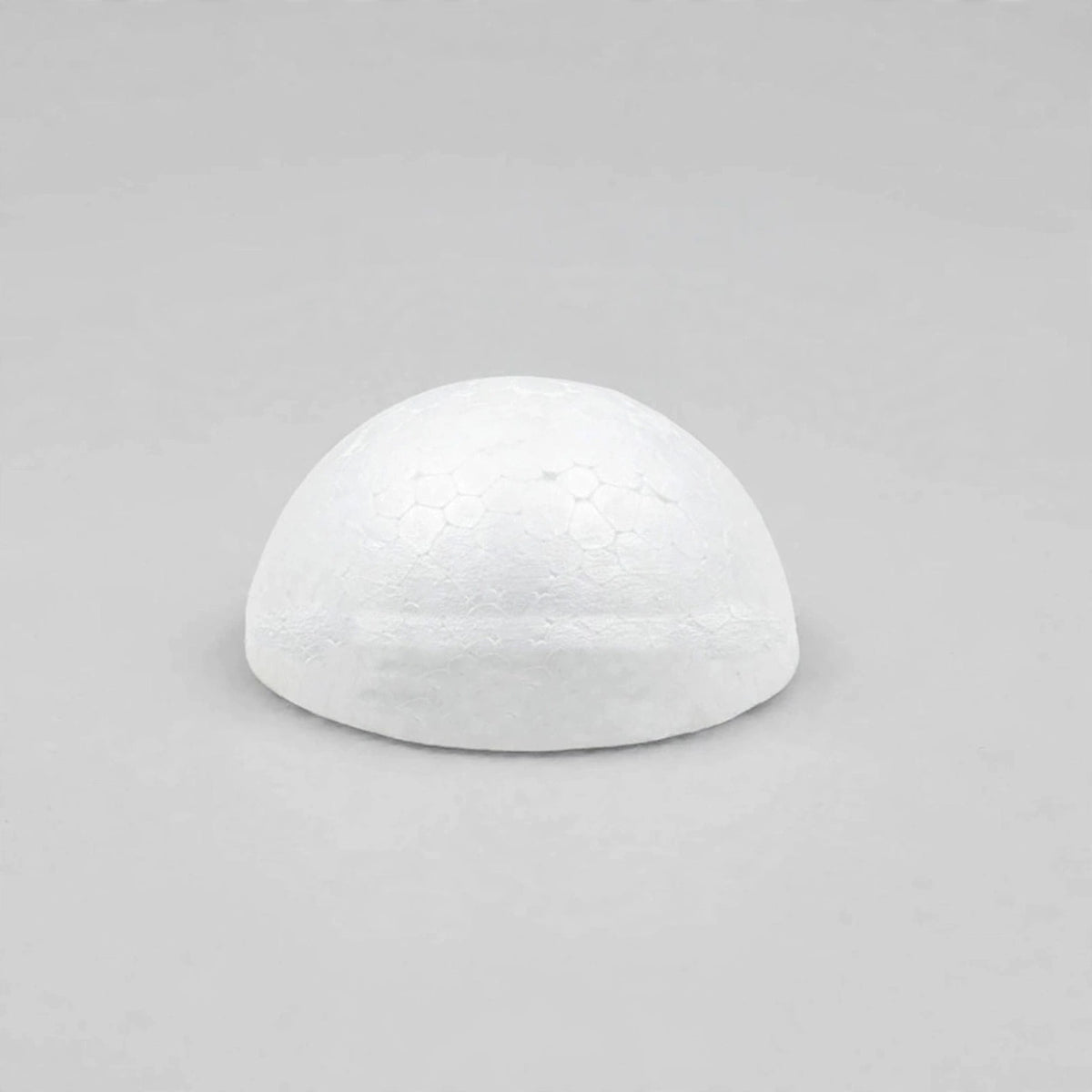A white foam half ball sits centered on a light gray surface with ample empty space around it.