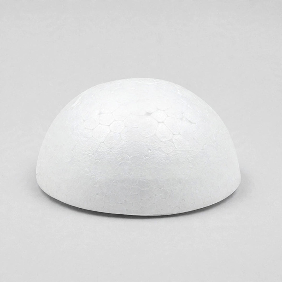 A white foam half ball rests flat-side down on a light gray surface, casting a narrow shadow beneath its edge.