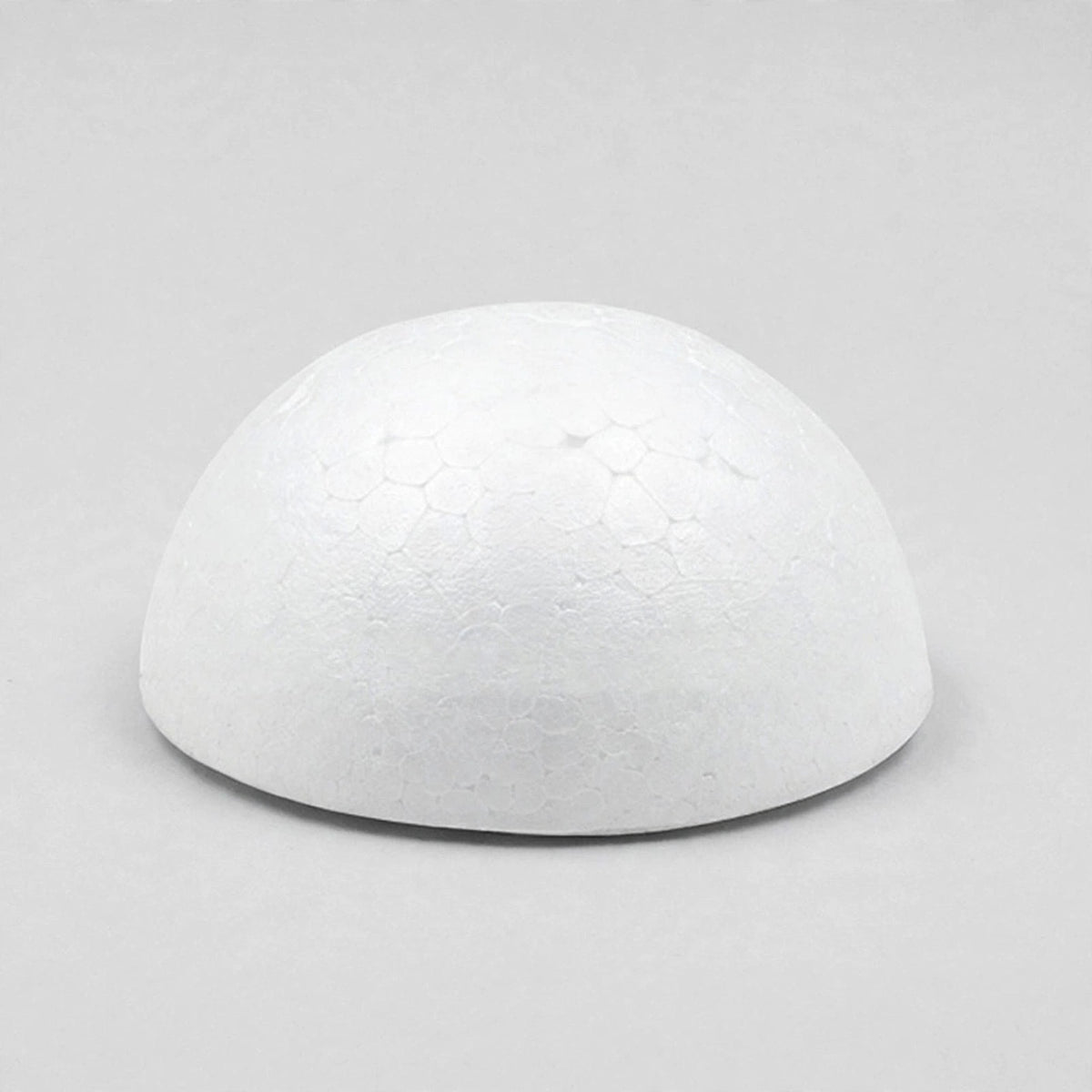A white foam half ball rests flat-side down on a light gray surface, casting a narrow shadow beneath its edge.