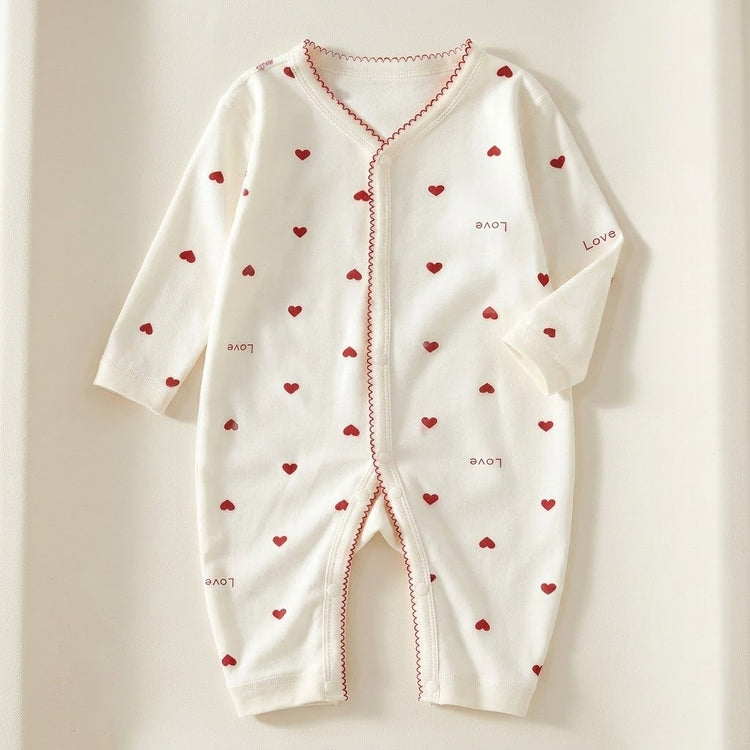 Cream long-sleeve baby romper with red hearts, Love lettering and red scalloped trim lies flat on a cream background.