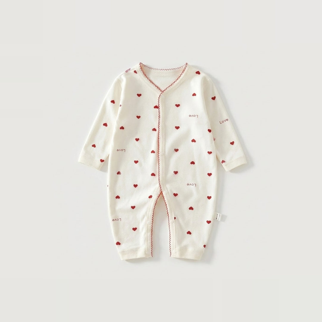 An off-white long-sleeve baby romper with a red heart pattern and red piping details, laid flat on a light gray background.