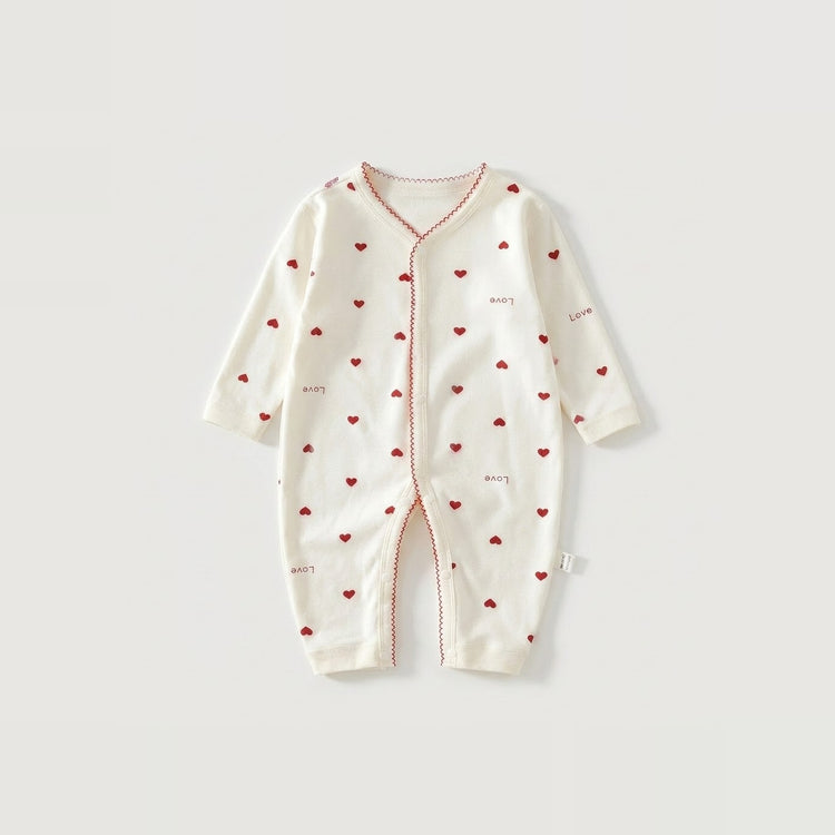 An off-white long-sleeve baby romper with a red heart pattern and red piping details, laid flat on a light gray background.