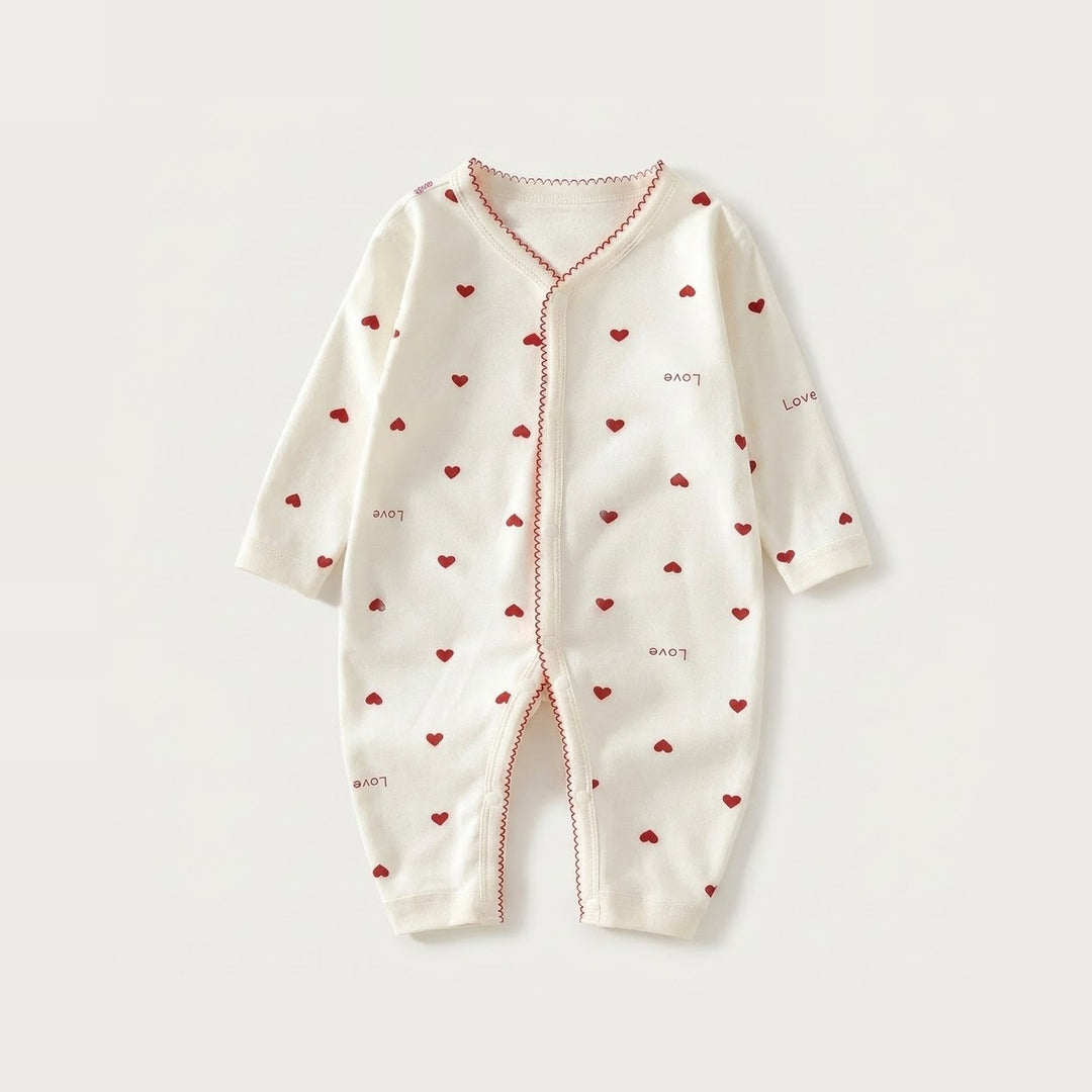 Cream long-sleeved baby romper with red hearts, scattered love lettering, and red scalloped trim lies flat on a pale background.