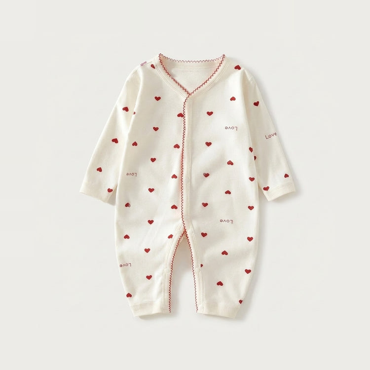 Cream long-sleeved baby romper with red hearts, scattered love lettering, and red scalloped trim lies flat on a pale background.
