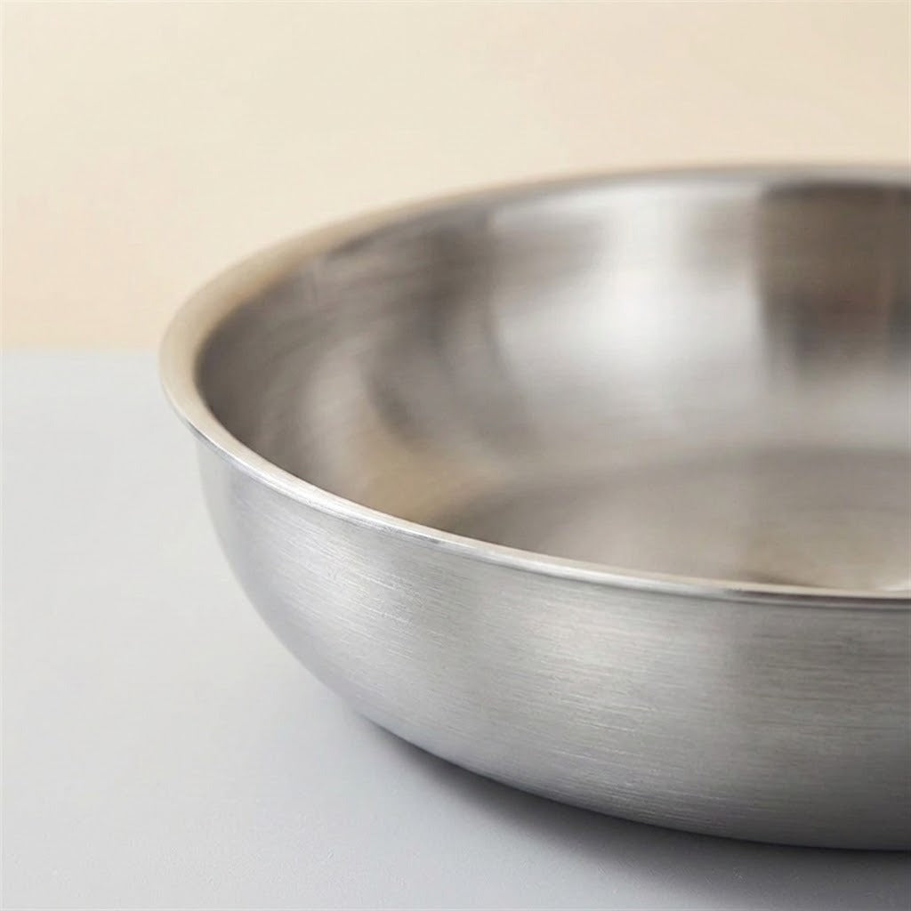 Close-up of a stainless steel paella pan showing its brushed exterior and rim against a warm beige background.