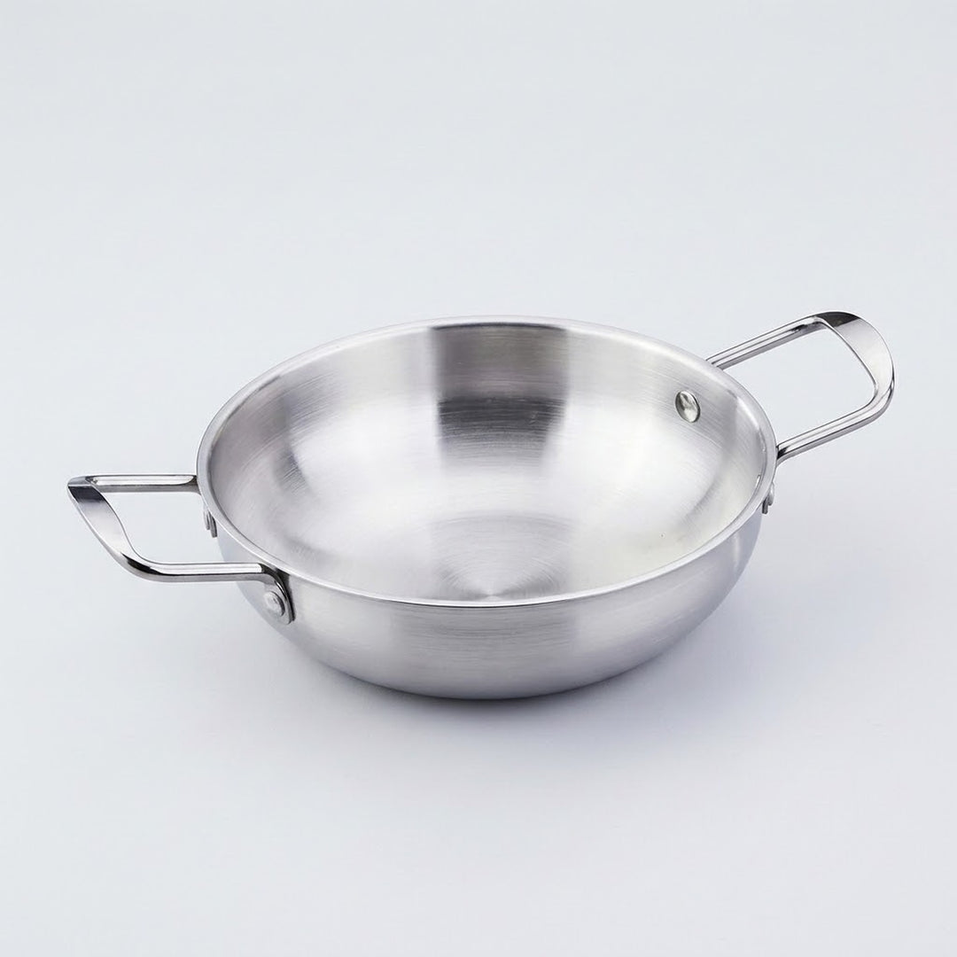A silver stainless steel paella pan with riveted side handles is shown close up against a light gray background.