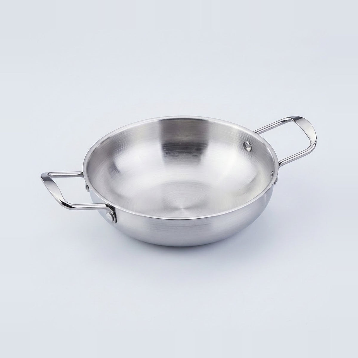 A silver stainless steel paella pan rests on a light gray background, showing its reflective interior and two loop handles.