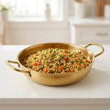 A gold-colored paella pan with two side handles holds colorful vegetable rice on a white kitchen countertop.