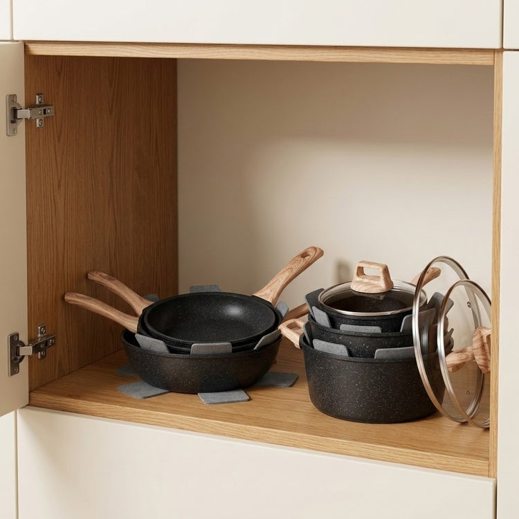 A set of black non-stick cookware, including frying pans with wooden handles and a saucepan with a glass lid, neatly arranged inside an open wooden kitchen cabinet.