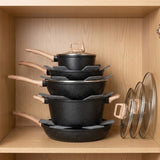 A set of five black speckled nonstick cookware pots and pans with light wood handles, neatly stacked inside a wooden cabinet next to two glass lids.