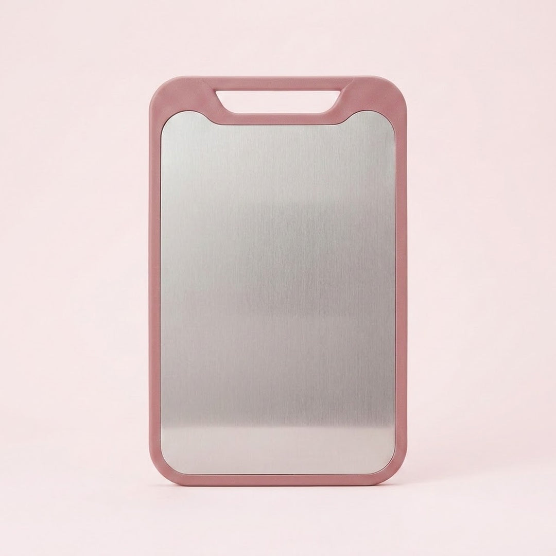 A pink cutting board with a stainless steel surface and integrated handle stands against a pale pink background.