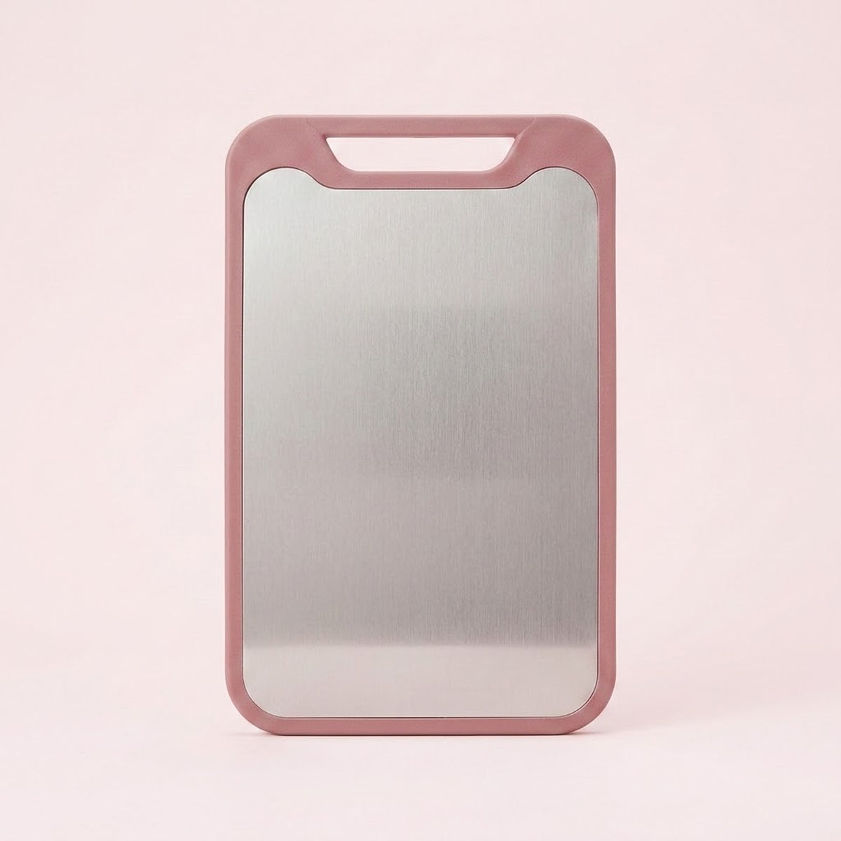 A pink cutting board with a stainless steel surface and integrated handle stands against a pale pink background.