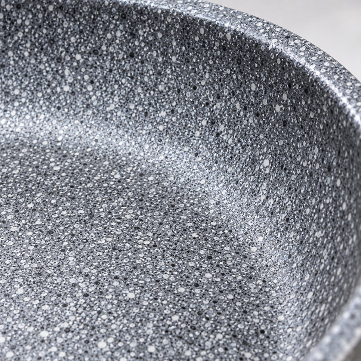 Macro detail of the smooth grey speckled non-stick cooking surface and curved pan rim.