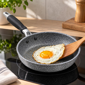 Non-stick frying pan cooks an egg cleanly on an induction hob in a bright home kitchen.