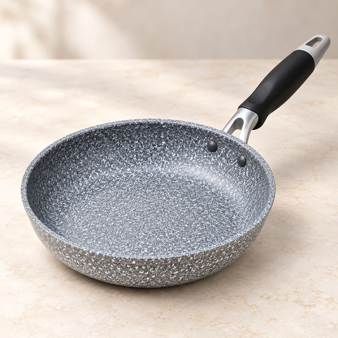 Grey speckled non-stick frying pan shown close up with its broad cooking surface and black handle.
