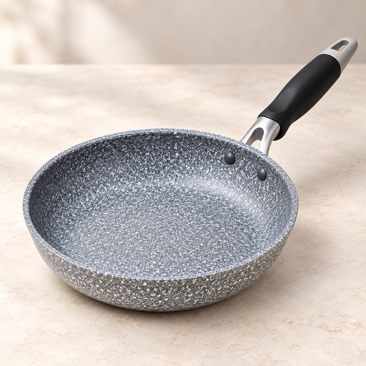 Grey speckled non-stick frying pan shown close up with its broad cooking surface and black handle.