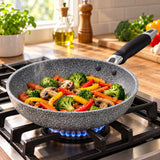 Grey speckled non-stick frying pan cooks vegetables over a gas flame in a home kitchen.