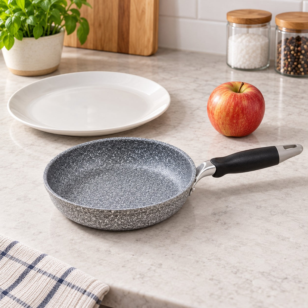 Compact grey speckled non-stick frying pan beside a dinner plate and apple for scale.
