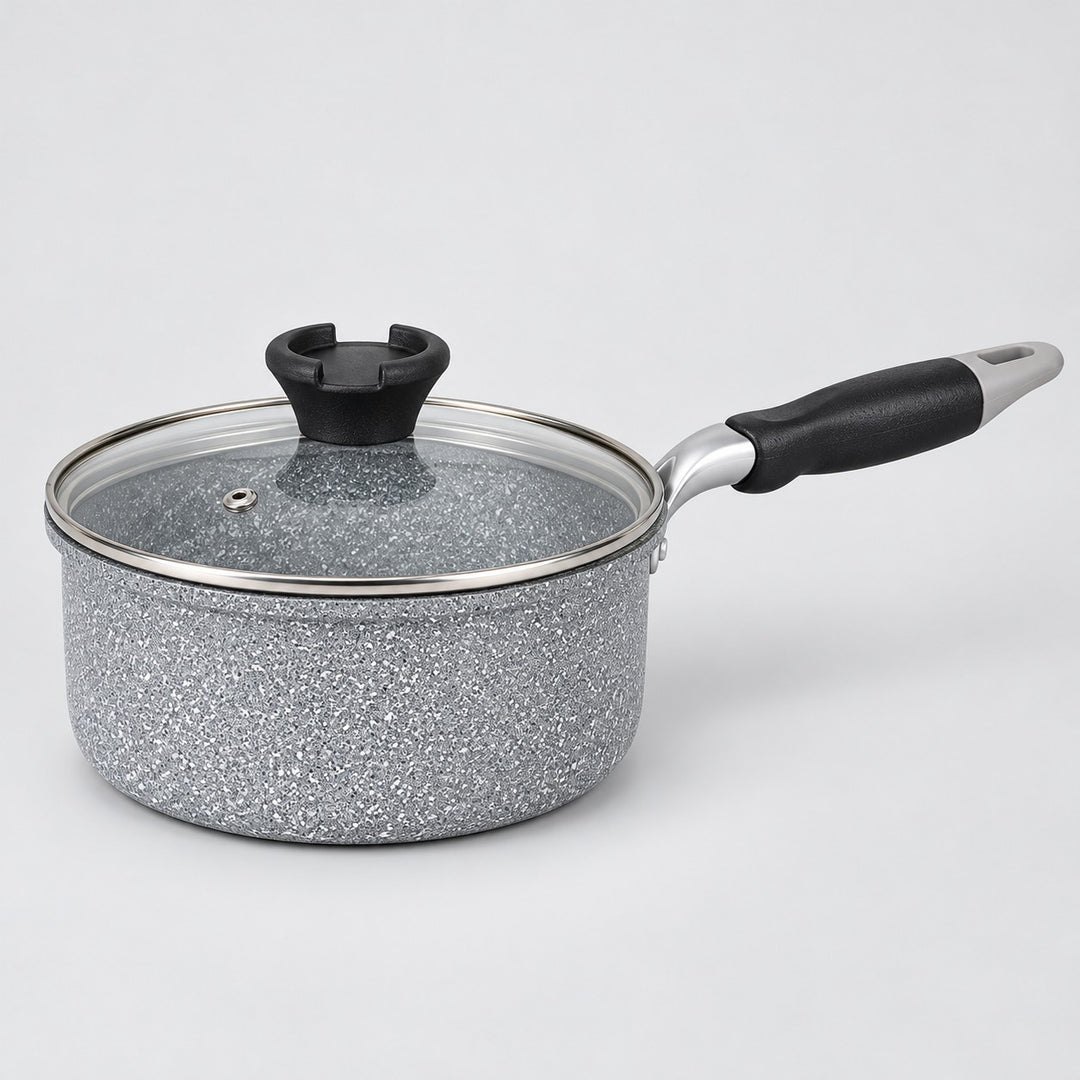 Grey speckled non-stick milk pot with glass lid and black handle shown on a pale studio background.