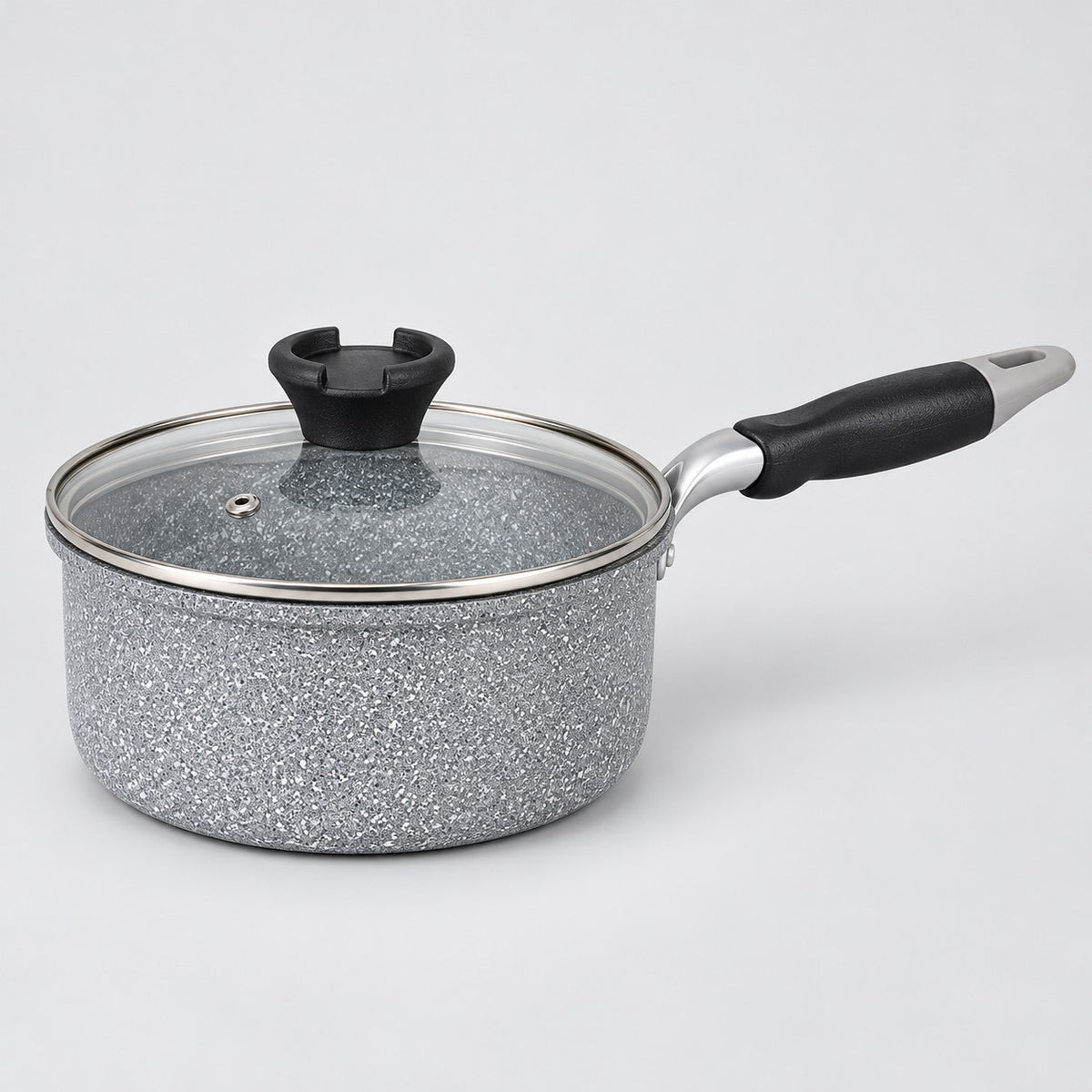 Grey speckled non-stick milk pot with glass lid and black handle shown on a pale studio background.