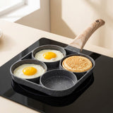Four-well speckled gray egg frying pan cooking two eggs and one pancake, with one empty well on a black cooktop.