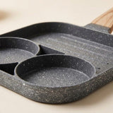 Close-up of a gray speckled egg frying pan showing two round wells and a ridged grill section on a cream surface.
