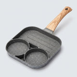 A gray speckled egg frying pan with two round wells, a ridged grill section and a wood-grain handle rests against a light background.