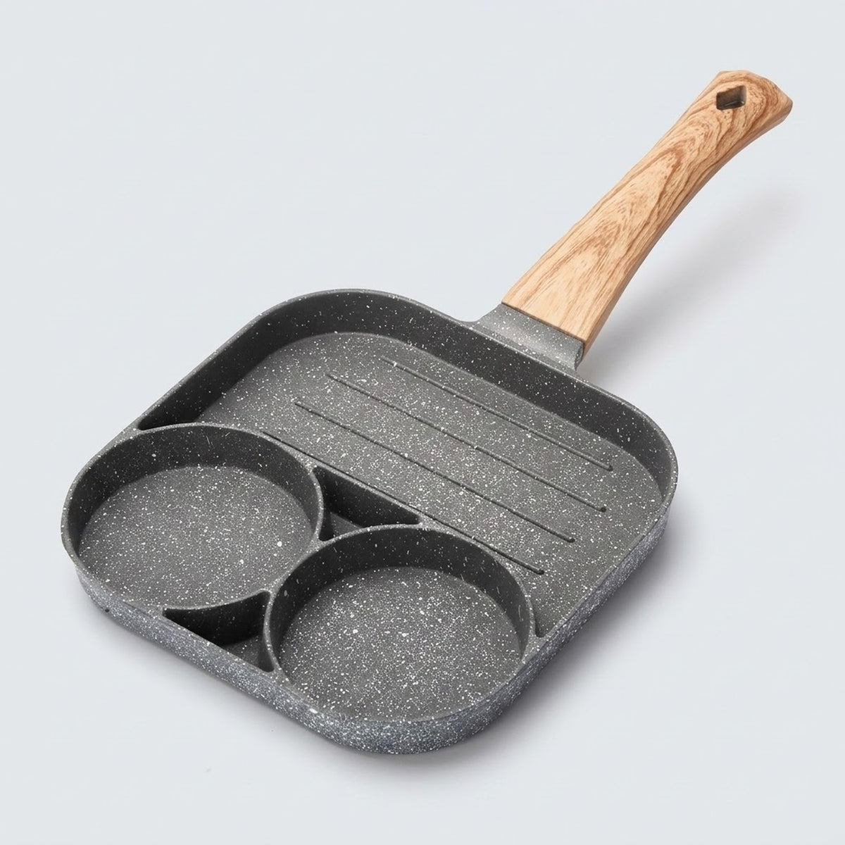 A gray speckled egg frying pan with two round wells, a ridged grill section and a wood-grain handle rests against a light background.