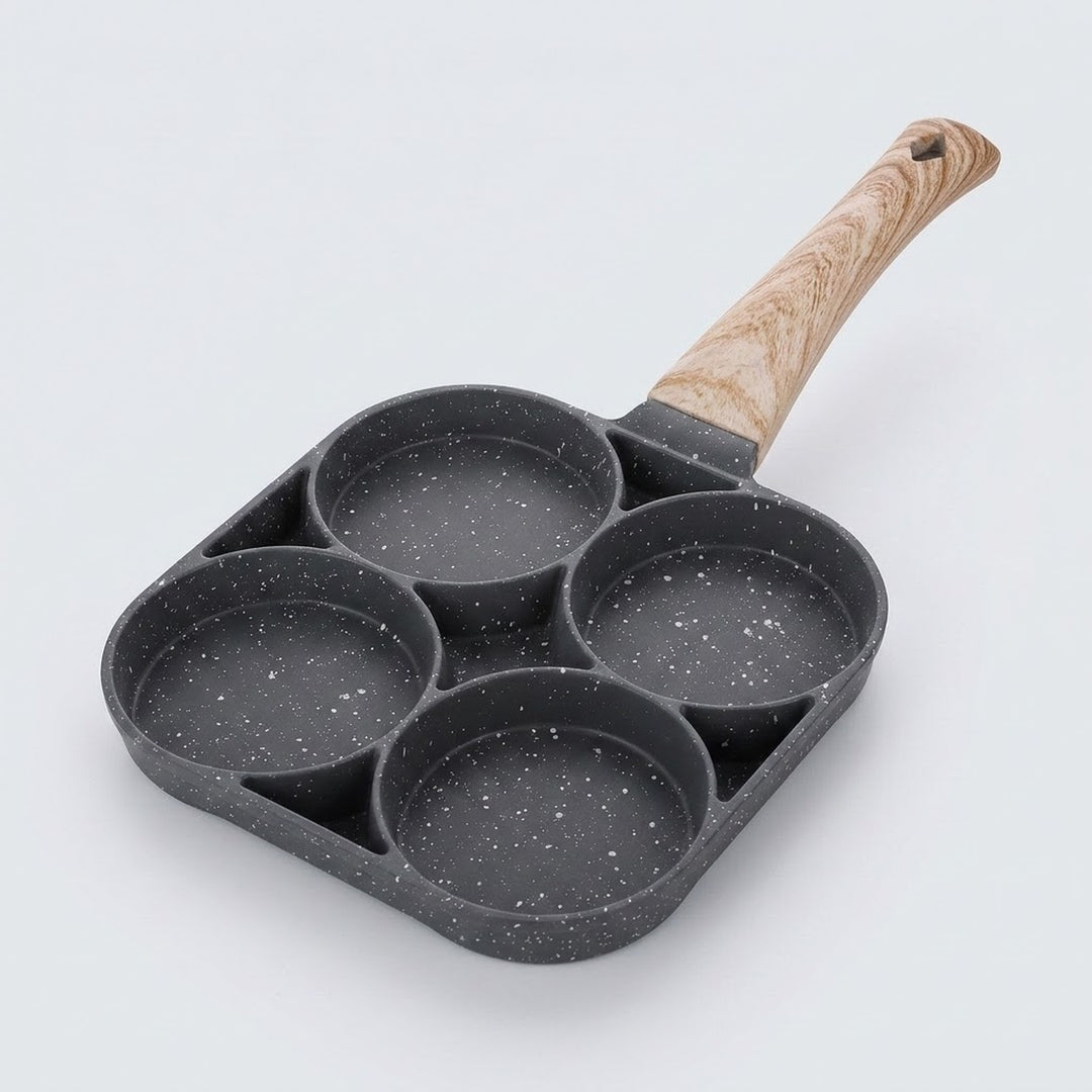A dark gray speckled egg frying pan with four round wells and a light wood-grain handle rests against a pale background.