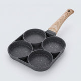 A dark gray speckled egg frying pan with four round wells and a light wood-grain handle rests against a pale background.