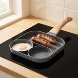 A gray speckled egg frying pan with a wood-grain handle holds an egg and two sausages on a black kitchen cooktop.