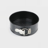 A black non-stick springform pan with a silver metal clasp and white release lever, shown on a light gray background.