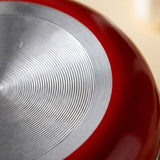 Close-up of a red frying pan underside with concentric grooves across its silver metal base against a cream background.