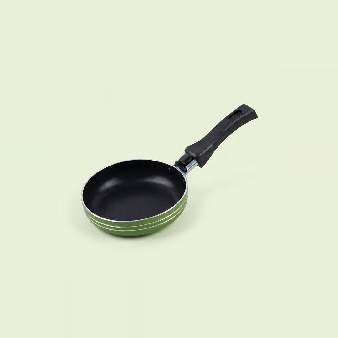 Green frying pan with a black nonstick interior, silver rim, and black hanging handle on a pale green background.