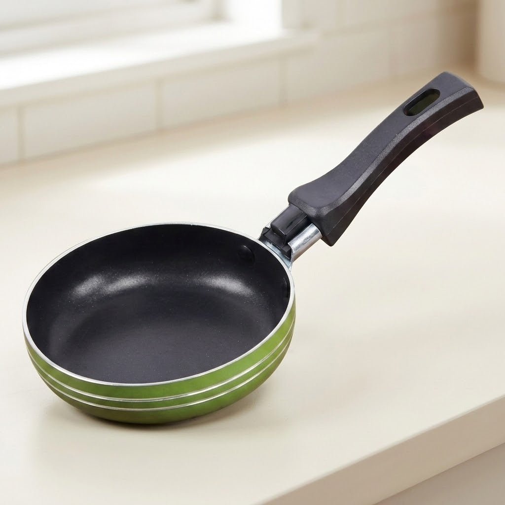 A non-stick frying pan with a black interior and a green exterior, featuring a black handle, resting on a light beige countertop near a window.