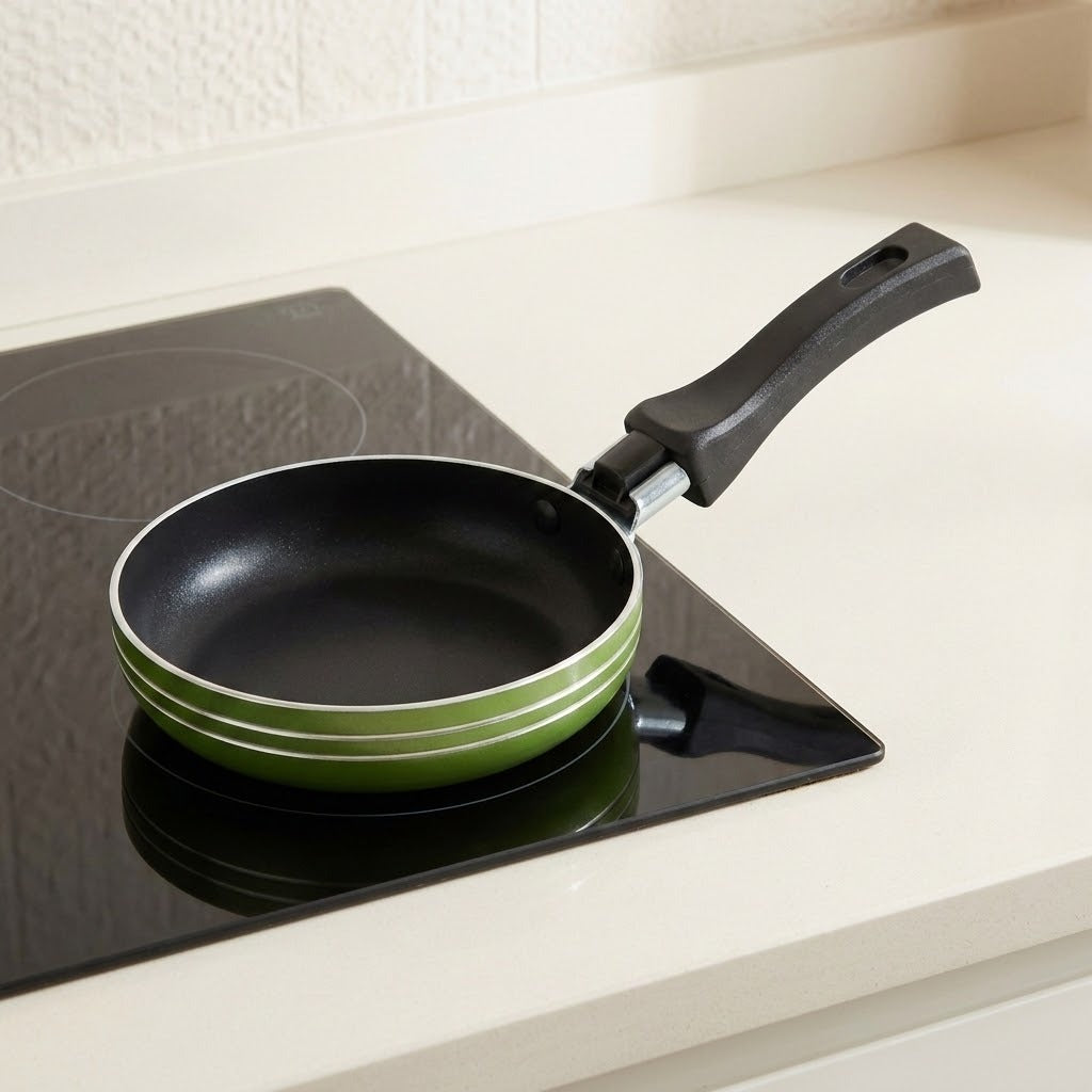 A small frying pan with a black interior and handle, featuring a light green exterior rim, resting on a black induction cooktop set in a kitchen countertop.