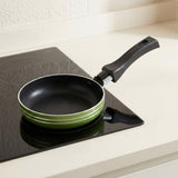 A small frying pan with a black interior and handle, featuring a light green exterior rim, resting on a black induction cooktop set in a kitchen countertop.