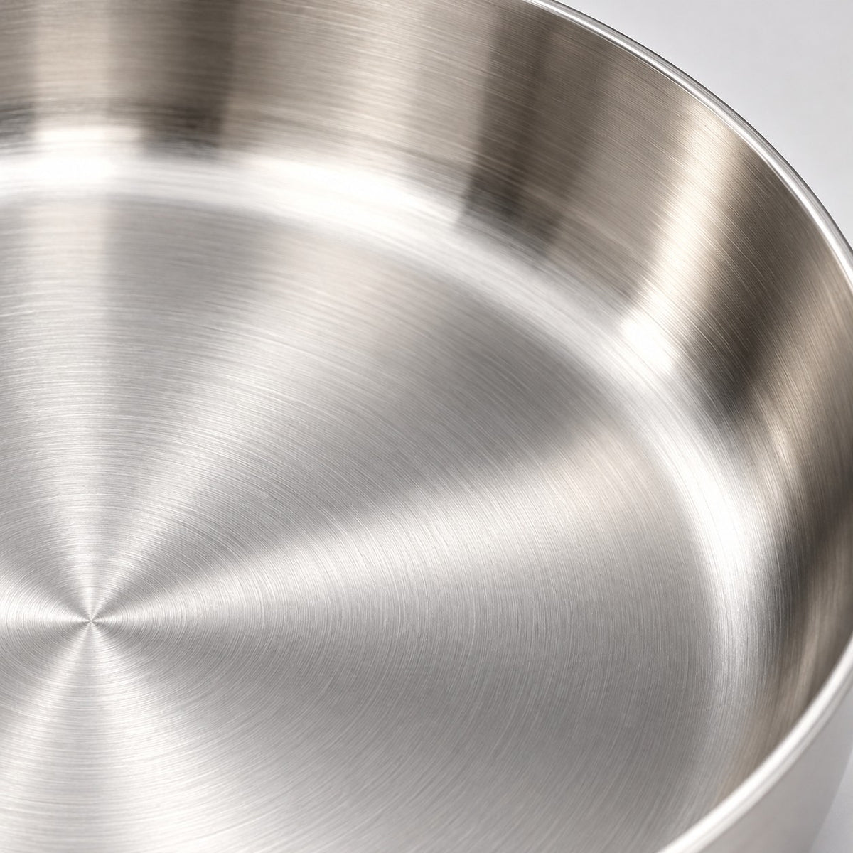 316 stainless steel frying pan macro showing the smooth reflective metal interior and curved rim.