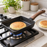 Japanese omelet pan cooks a small pancake on a gas cooktop beside a breakfast plate.