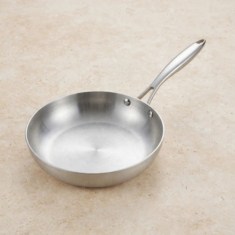 Empty silver metal frying pan with a long riveted handle rests on a beige speckled countertop.