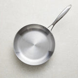 Empty silver metal frying pan viewed from above on a pale speckled countertop, with its handle pointing upper right.