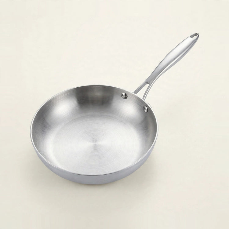 A silver metal frying pan with curved sides and two visible handle rivets rests against a plain cream background.