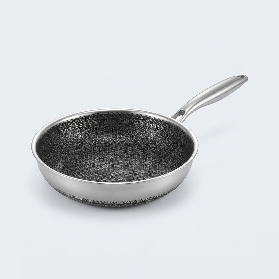 Stainless steel frying pan with a dark honeycomb interior and long silver handle on a light gray background.