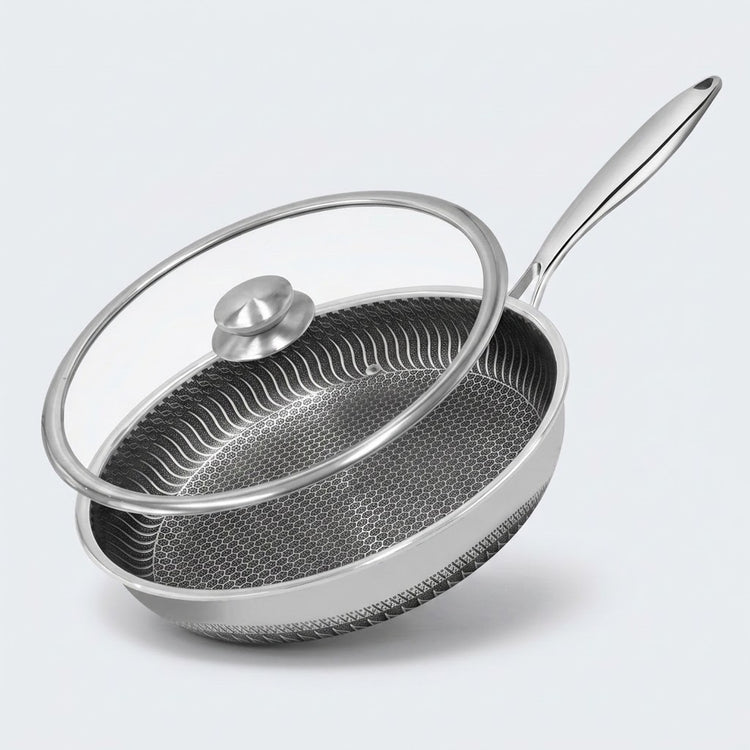 Stainless steel frying pan with a honeycomb interior and tilted glass lid with a silver knob on a light gray background.