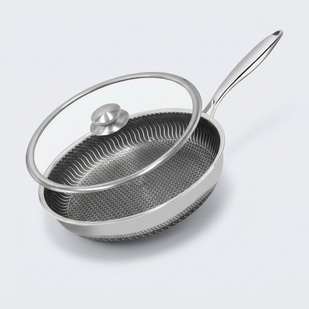 A stainless steel frying pan with a textured non-stick interior and a clear glass lid with a silver knob, shown on a light gray background.