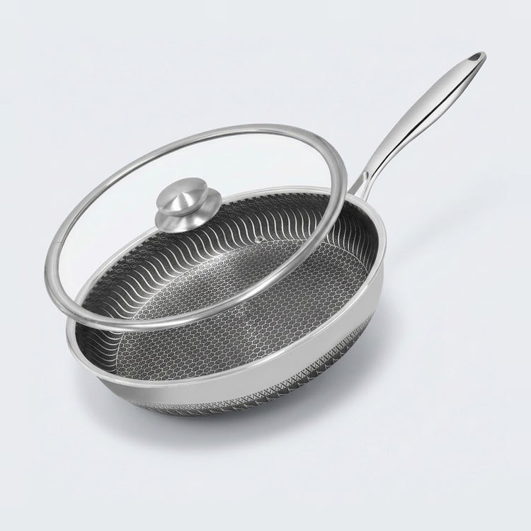 A stainless steel frying pan with a textured non-stick interior and a clear glass lid with a silver knob, shown on a light gray background.