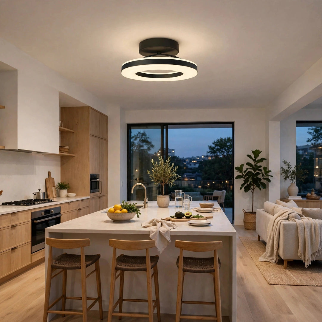 A modern circular LED ceiling light with black rings and a white illuminated diffuser, hanging in a bright, contemporary kitchen and living room setting.