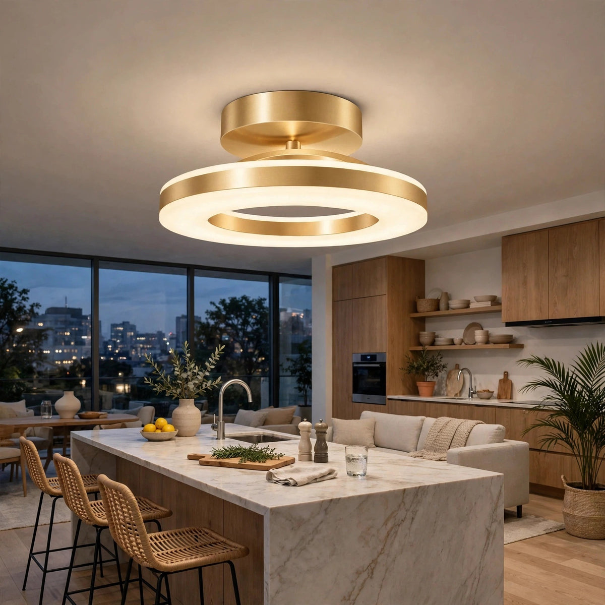 A modern semi-flush mount ceiling light fixture with two concentric circular rings in brushed gold and warm white LED lighting, installed in a contemporary kitchen with wood cabinets, a marble island, and a city view at dusk.