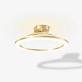 A modern semi-flush mount ceiling light fixture with a circular gold-toned metal frame and a warm white illuminated diffuser, shown against a clean white background with a soft shadow.