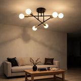A black and gold-toned chandelier with six glowing white globe bulbs hangs above a cream sofa and wooden coffee table.